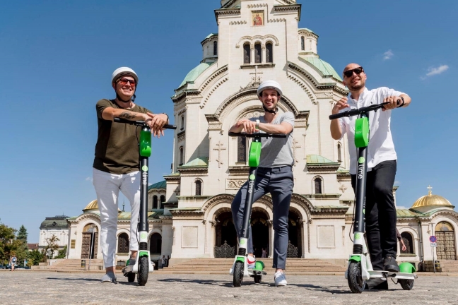 Three people smiling as they stand on their E-scooters in Sofia, Bulgaria.